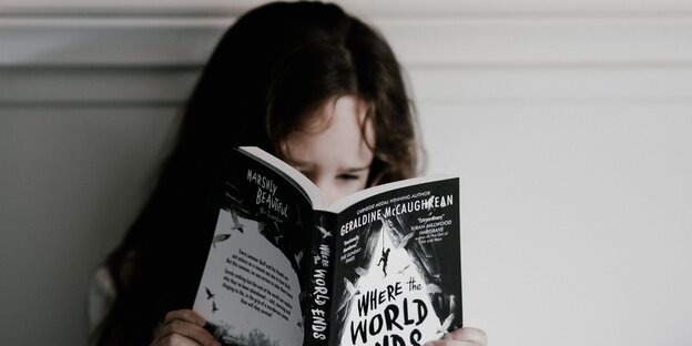 Ein Mädchen mit langen dunklen Haaren hat das Gesicht hinter einem Buch mit schwarzem Cover verborgen Ein Mädchen mit langen dunklen Haaren hat das Gesicht hinter einem Buch mit schwarzem Cover verborgen