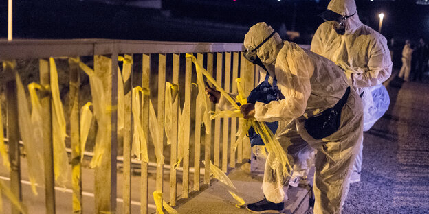 Zwei Menschen in Schutzanzügen ziehen an Papierbändern, die an einer Brücke festgebunden sind Zwei Menschen in Schutzanzügen ziehen an Papierbändern, die an einer Brücke festgebunden sind