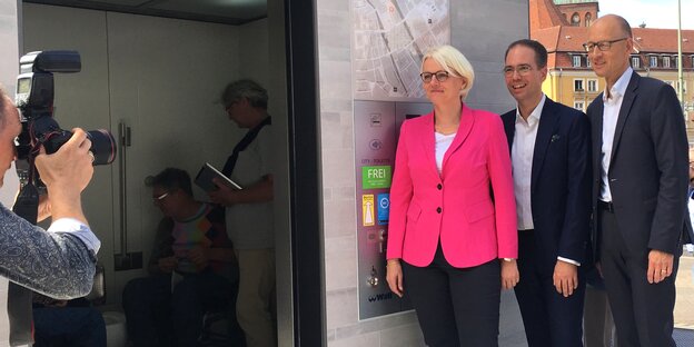 Eine Frau und zwei Männer werden vor einer öffentlichen Toilette fotografiert Eine Frau und zwei Männer werden vor einer öffentlichen Toilette fotografiert