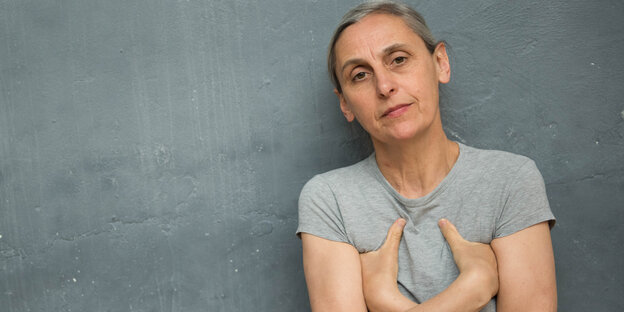 Eine Frau im grauen T-Shirt lehnt an einer grauen Wand Eine Frau im grauen T-Shirt lehnt an einer grauen Wand