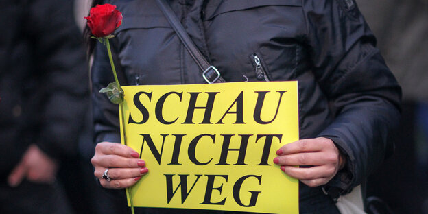 Eine Person hält eine Rose und ein Schild mit der Aufschrift "Schau nicht weg" in der Hand Eine Person hält eine Rose und ein Schild mit der Aufschrift "Schau nicht weg" in der Hand