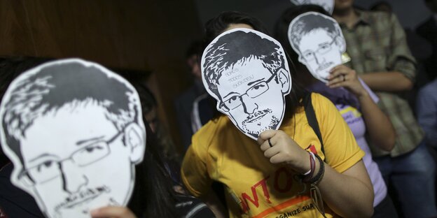 Menschen, die sich aus Pappe ausgeschnittene Masken von Edward Snowden vor Ihr Gesicht halten. Menschen, die sich aus Pappe ausgeschnittene Masken von Edward Snowden vor Ihr Gesicht halten.