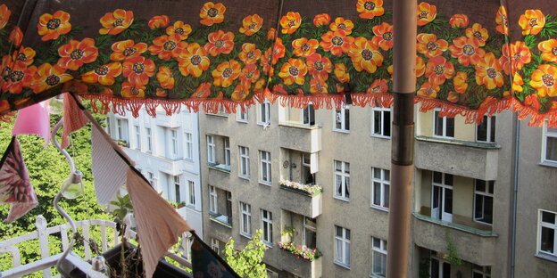 Blick von einem Balkon auf eine Häuserfront, oben begrenzt von einem Sonnenschirm mit Blumenmuster Blick von einem Balkon auf eine Häuserfront, oben begrenzt von einem Sonnenschirm mit Blumenmuster