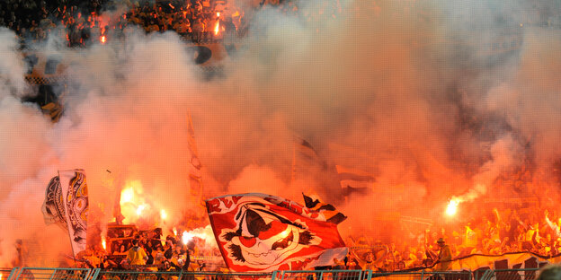 Die Fankurve der Dynamo Dresden Fans im orangen Licht zahlreicher gezündeter Bengalos Die Fankurve der Dynamo Dresden Fans im orangen Licht zahlreicher gezündeter Bengalos