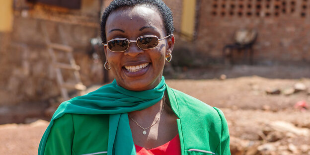 Victoire Ingabire lächelt in die Kamera, sie trägt ein rotes Oberteil und Jacke und Schal in grün Victoire Ingabire lächelt in die Kamera, sie trägt ein rotes Oberteil und Jacke und Schal in grün
