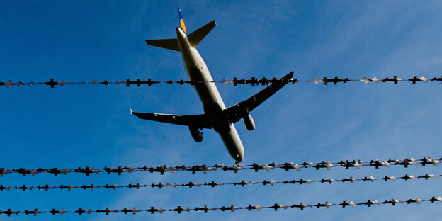 Ein Flugzeug überfliegt einen Stacheldrahtzaun. Ein Flugzeug überfliegt einen Stacheldrahtzaun.