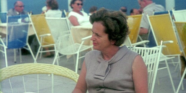Eine Frau mittleren Alters sitzt auf einer Terrasse mit Tischen und Stühlen Eine Frau mittleren Alters sitzt auf einer Terrasse mit Tischen und Stühlen
