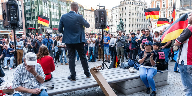 Eine Menschentraube steht mit Deutschlandfahnen vor einem Redner Eine Menschentraube steht mit Deutschlandfahnen vor einem Redner