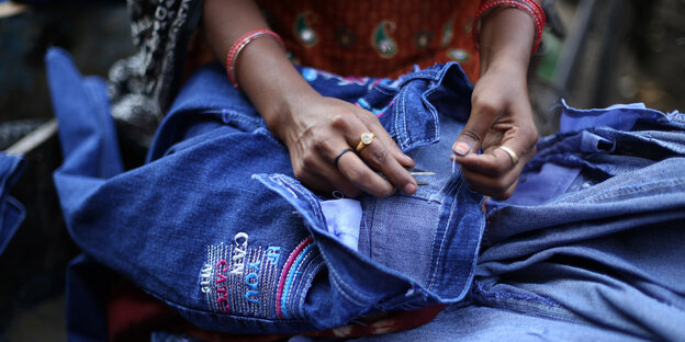 Eine Frau näht Aufnäher auf eine Jeans Eine Frau näht Aufnäher auf eine Jeans