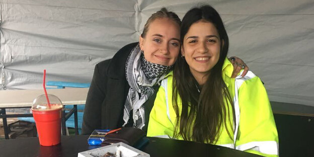 Zwei junge Frauen sitzen an einem Tisch und lächeln in die Kamera Zwei junge Frauen sitzen an einem Tisch und lächeln in die Kamera