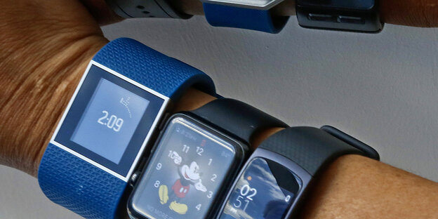 Drei blaue Armbänder mit so genannten Fitness Trackern umschließen einen Arm Drei blaue Armbänder mit so genannten Fitness Trackern umschließen einen Arm