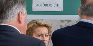 Verteidigungsministerin Ursula von der Leyen (CDU) blickt zwischen den Schultern zweier Jackettträger hindurch.