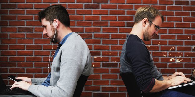 Zwei Männer sitzen mit dem Rücken zueinander an ihren Laptops Zwei Männer sitzen mit dem Rücken zueinander an ihren Laptops