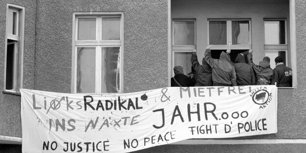 Hausbesetzer stehen auf einem Balkon vor einem Plakat