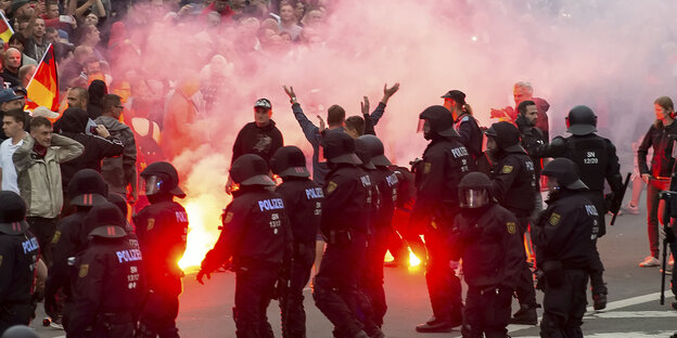 Polizisten vor einer Masse von Menschen. Es sind Bengalos gezündet