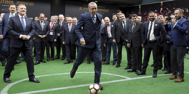 Recep Tayyip Erdoğan schießt einen Fußball, sehr viele Männer in Anzügen schauen ihm dabei zu Recep Tayyip Erdoğan schießt einen Fußball, sehr viele Männer in Anzügen schauen ihm dabei zu