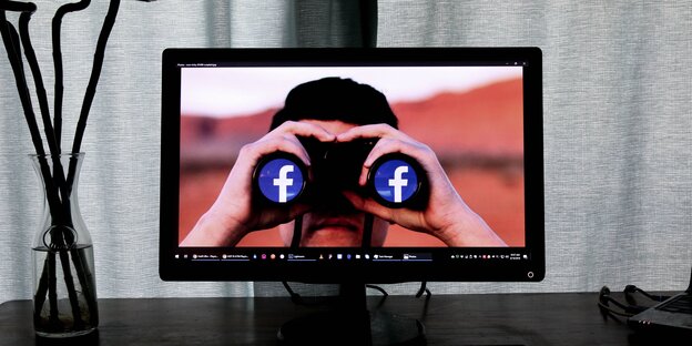 Ein Mann ist auf einem Bildschirm zu sehen, er hält sich ein Fernglas vor die Augen, in dessen Linsen das Facebook-Logo prangt Ein Mann ist auf einem Bildschirm zu sehen, er hält sich ein Fernglas vor die Augen, in dessen Linsen das Facebook-Logo prangt