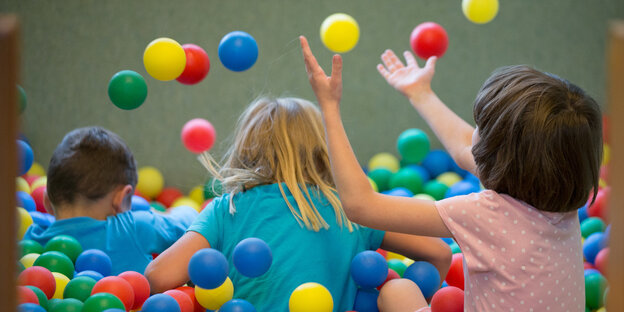 Drei Kinder, von hinten zu sehen, spielen in einem Bällebad Drei Kinder, von hinten zu sehen, spielen in einem Bällebad
