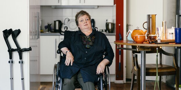 Eine Frau sitzt schief in einem Rollstuhl in ihrer Küche Eine Frau sitzt schief in einem Rollstuhl in ihrer Küche