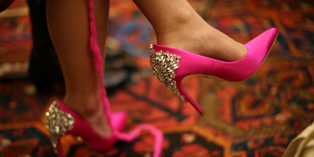 Pinke hochhackige Schuhe mit silberner Verzierung. Daneben hängt ein pinker Wollfaden herunter. Die Frau, die die Schuhe trägt strickt einen sogenannten „Pussyhat“, eine pinke Mütze Pinke hochhackige Schuhe mit silberner Verzierung. Daneben hängt ein pinker Wollfaden herunter. Die Frau, die die Schuhe trägt strickt einen sogenannten „Pussyhat“, eine pinke Mütze