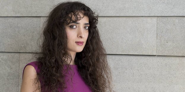 Eine junge Frau mit langen braunen Haaren steht vor einer Steinwand Eine junge Frau mit langen braunen Haaren steht vor einer Steinwand