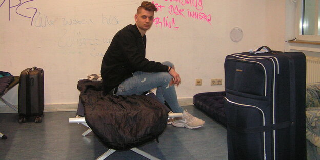 Junger Mann sitzt auf Feldbett Junger Mann sitzt auf Feldbett