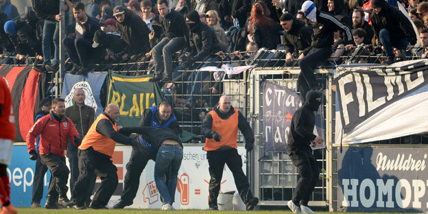 Fußball-Fans klettern über eine Absperrung zum Spielfeld. Fußball-Fans klettern über eine Absperrung zum Spielfeld.
