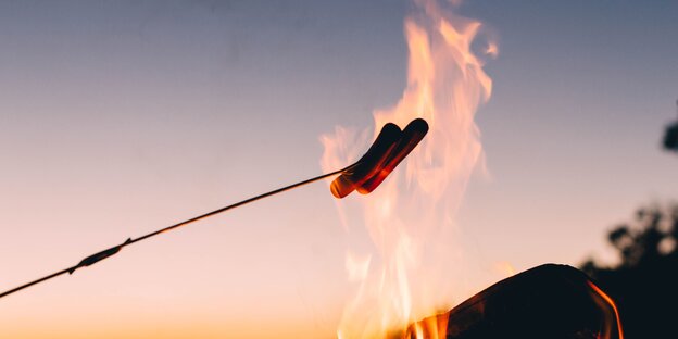 zwei Würstchen rösten auf einen Stock gespießt über offenem Feuer zwei Würstchen rösten auf einen Stock gespießt über offenem Feuer