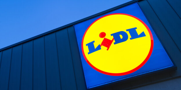 Das Logo eines Lidl-Supermarktes in Berlin-Reinickendorf leuchtet vor dem Abendhimmel