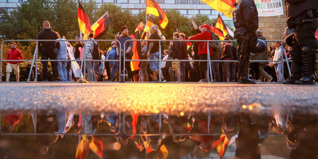 Demonstranten stehen mit Deutschlandflaggen vor einem Gitter, daneben Polizisten Demonstranten stehen mit Deutschlandflaggen vor einem Gitter, daneben Polizisten
