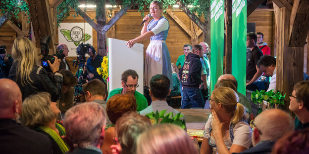Eine Frau im Dirndl redet im Bierzelt, dahinter Grüne Parteiwerbung Eine Frau im Dirndl redet im Bierzelt, dahinter Grüne Parteiwerbung