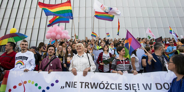 Viele Menschen mit bunten Fahnen stehen hinter einem Banner Viele Menschen mit bunten Fahnen stehen hinter einem Banner