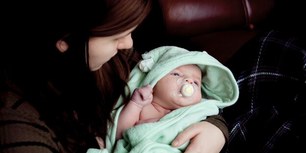 Eine Frau hält ein Baby, das in ein türkisfarbenes Handtuch gehüllt ist Eine Frau hält ein Baby, das in ein türkisfarbenes Handtuch gehüllt ist