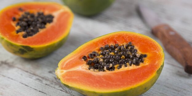 Eine aufgeschnittene Papaya liegt neben einem Messer auf einem Tisch Eine aufgeschnittene Papaya liegt neben einem Messer auf einem Tisch