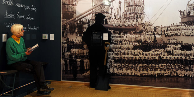 Eine Frau sitzt im Marinemuseum Wilhelmshaven in einer Ausstellungsszene.