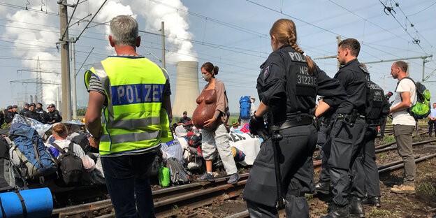Aktivisten des Anti-Braunkohle-Bündnisses "Ende Gelände" blockieren Schienen, im Hintergrund ist ein Kraftwerk, im Vordergrund steht Polizei Aktivisten des Anti-Braunkohle-Bündnisses "Ende Gelände" blockieren Schienen, im Hintergrund ist ein Kraftwerk, im Vordergrund steht Polizei