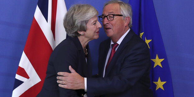 Ein Mann und eine Frau begrüßen sich mit Wangenküsschen, im Hintergrund die Flaggen von Großbritannien und der Europäischen Union Ein Mann und eine Frau begrüßen sich mit Wangenküsschen, im Hintergrund die Flaggen von Großbritannien und der Europäischen Union