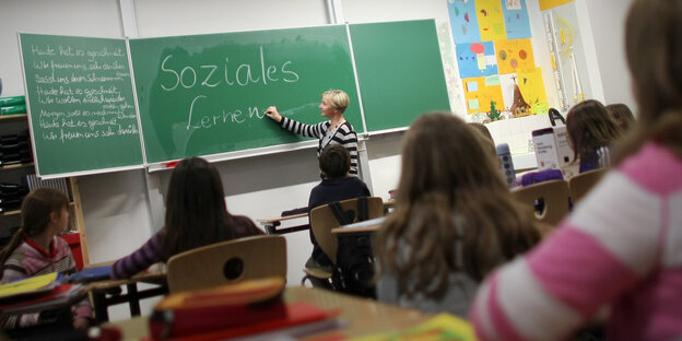 Eine Lehrerin steht vor einer Schulklasse an der Tafel.