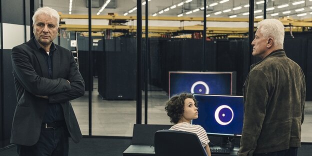 Zwei Männer stehen neben einer Frau, die vor einem Computerbildschirm sitzt Zwei Männer stehen neben einer Frau, die vor einem Computerbildschirm sitzt