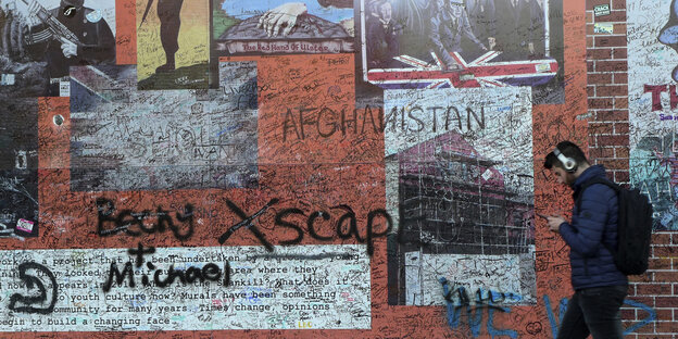 Ein Mann läuft vor einer Wand entlang, die mit Graffitis besprüht ist und schaut auf sein Handy Ein Mann läuft vor einer Wand entlang, die mit Graffitis besprüht ist und schaut auf sein Handy
