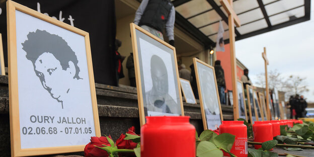 Mehrere gerahmte Bilder stehen nebeneinander, davor Grablichter und rote Rosen Mehrere gerahmte Bilder stehen nebeneinander, davor Grablichter und rote Rosen