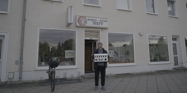 Georg Genoux steht vor einer Kneipe und trägt das Bühnenbild vor sich Georg Genoux steht vor einer Kneipe und trägt das Bühnenbild vor sich