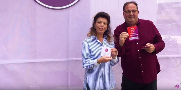 Eine Frau und ein Mann halten Werbeflyer vor einer violetten Wand Eine Frau und ein Mann halten Werbeflyer vor einer violetten Wand
