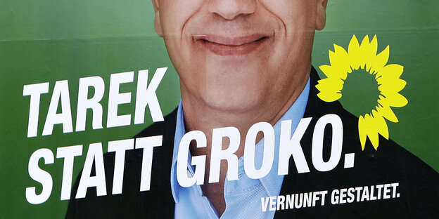 Auf einem grünen Plakat ist die untere Hälfte des Kopfes eines grinsenden Mannes zu sehen, quer darüber steht „Tarek statt Groko.“ Auf einem grünen Plakat ist die untere Hälfte des Kopfes eines grinsenden Mannes zu sehen, quer darüber steht „Tarek statt Groko.“
