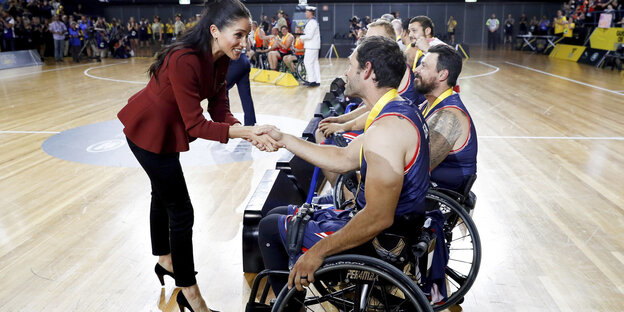 Eine junge Frau, Meghan, Herzogin von Sussex, reicht einem Mann, der in einem Rollstuhl sitzt, die Hand Eine junge Frau, Meghan, Herzogin von Sussex, reicht einem Mann, der in einem Rollstuhl sitzt, die Hand