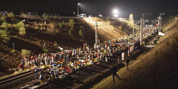 Es ist Nacht und viele Menschen stehen auf oder um ein Bahngleis Es ist Nacht und viele Menschen stehen auf oder um ein Bahngleis