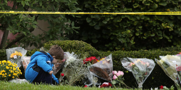 Eine Junge legt Blumen an eine Gedenkstelle, an der schon andere Blumen liegen, über ihm ein gelbes Polizei-Absperr-Band Eine Junge legt Blumen an eine Gedenkstelle, an der schon andere Blumen liegen, über ihm ein gelbes Polizei-Absperr-Band