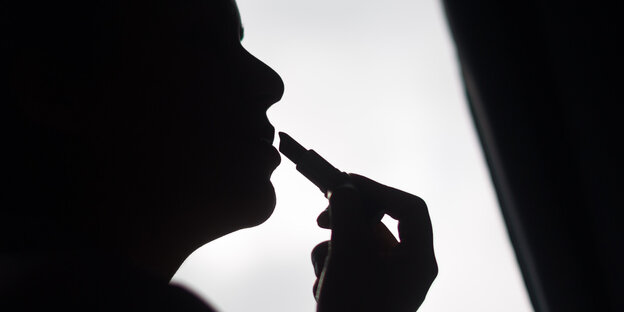 Schattenriss einer Person, die sich Lippenstift aufträgt. Schattenriss einer Person, die sich Lippenstift aufträgt.
