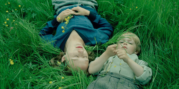 Zwei Kinder liegen auf dem Rücken im Gras.