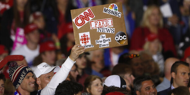 Aus einer Menschenmenge wird ein Schild mit der Aufschrift "Fake News" hochgehalten Aus einer Menschenmenge wird ein Schild mit der Aufschrift "Fake News" hochgehalten